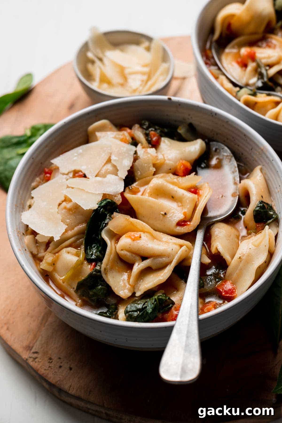 Tortellini soup in bowl with spoon, spinach and parmesan cheese on top.
