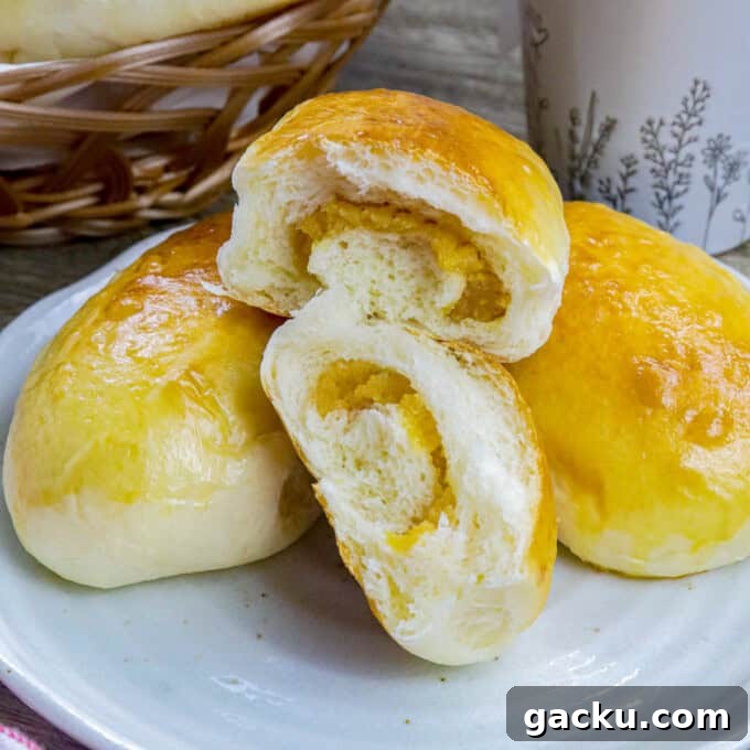 Yema Bread Rolls Recipe — Soft Filipino Custard-Filled Buns 8 Filipino custard buns on a white plate with a basket of bread rolls and cup of coffee in the background.