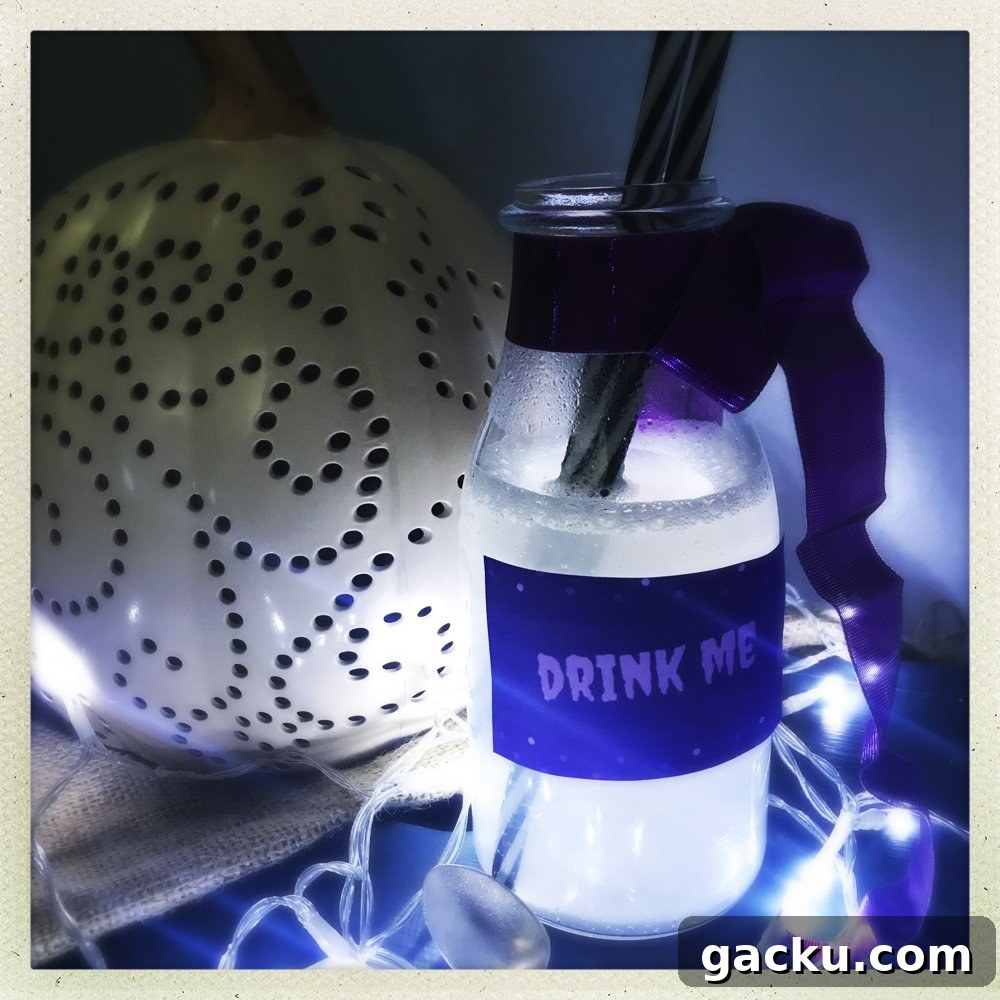 bottle of silver Halloween mocktail drink with label on saying Drink Me, white pumpkin in background.