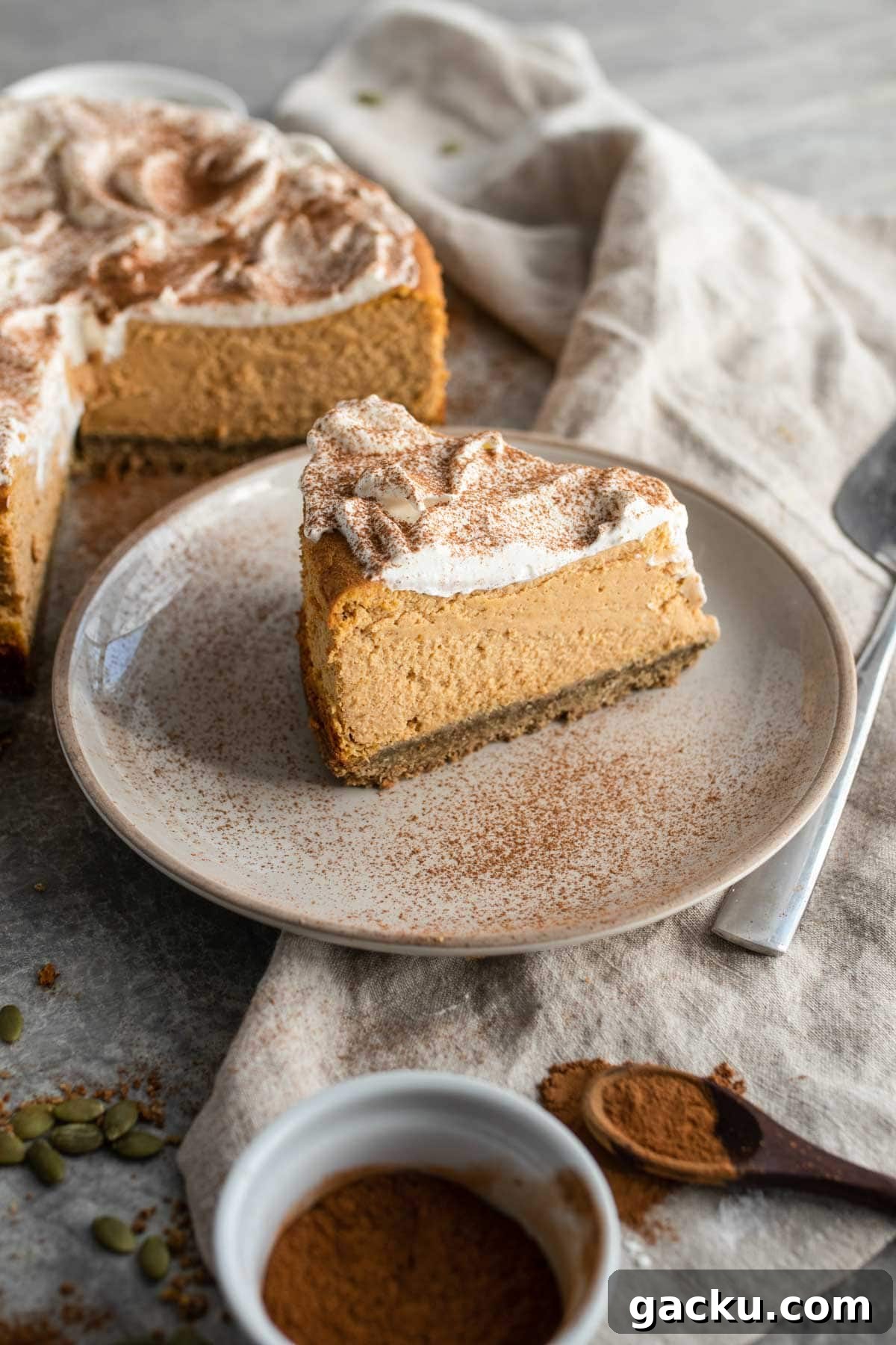 A pumpkin cheesecake slice on a plate dusted with cinnamon.
