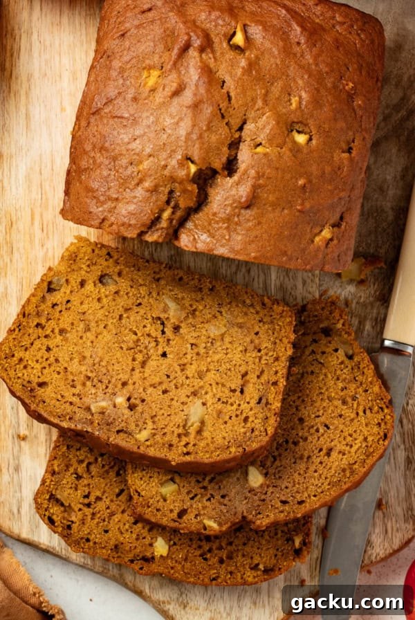 Slices of apple pumpkin bread on a serving platter next to a large loaf of the bread in the background.