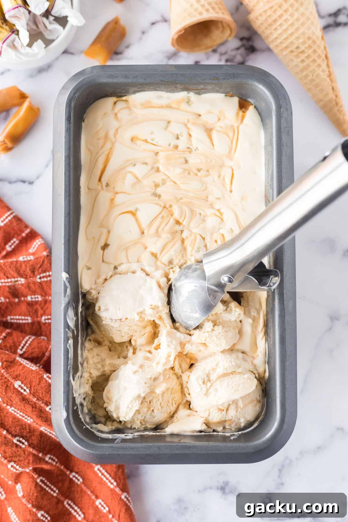 Salted caramel ice cream in a rectangular, metal serving dish with an ice cream scooper.