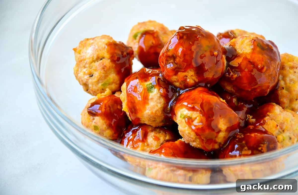 Baked chicken meatballs in a large glass mixing bowl with teriyaki sauce poured on top of them.