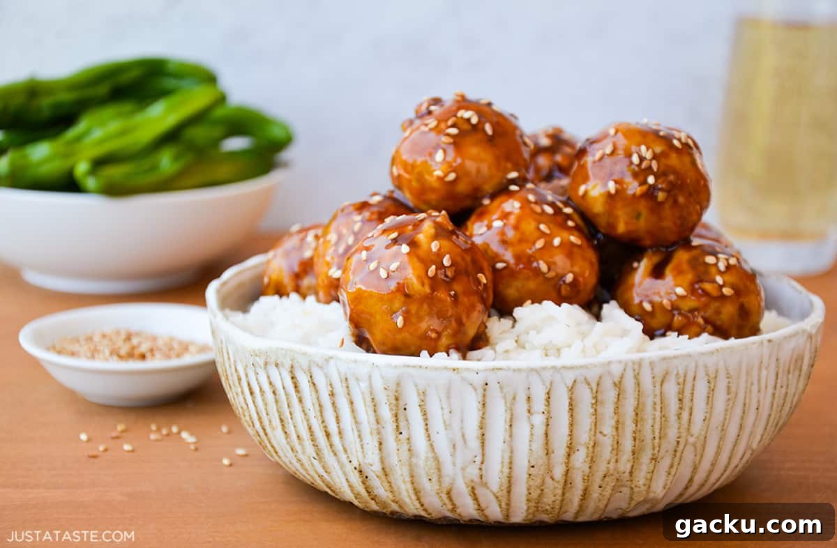 A bowl with white rice and chicken teriyaki meatballs with sesame seeds sprinkled on top.