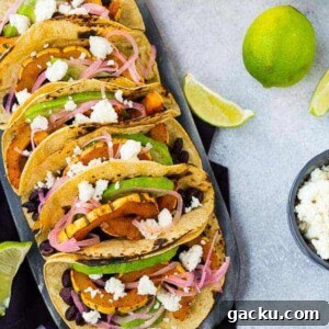 Delicata Squash & Black Bean Vegetarian Tacos for Fall Flavor 6 Overhead of several prepared tacos, lined up on decorative surface.