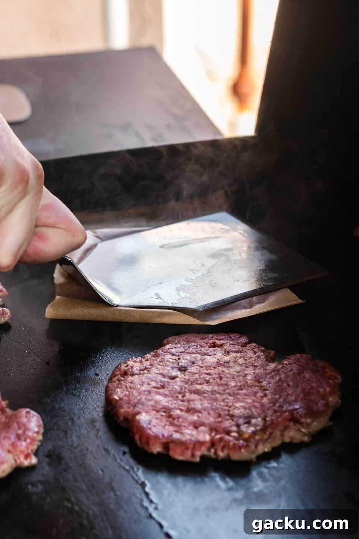 Perfect Blackstone Patty Melt Recipe: Juicy, Griddled Sandwich 9 Placing patties on Blackstone griddle and pressing down on parchment paper with spatula for Blackstone Patty Melts