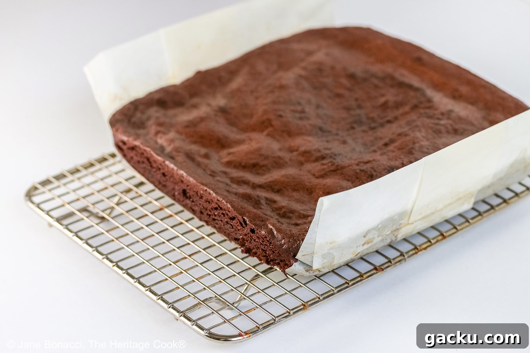 Whole block of brownies with a parchment sling, sitting on a wire cooling rack. 