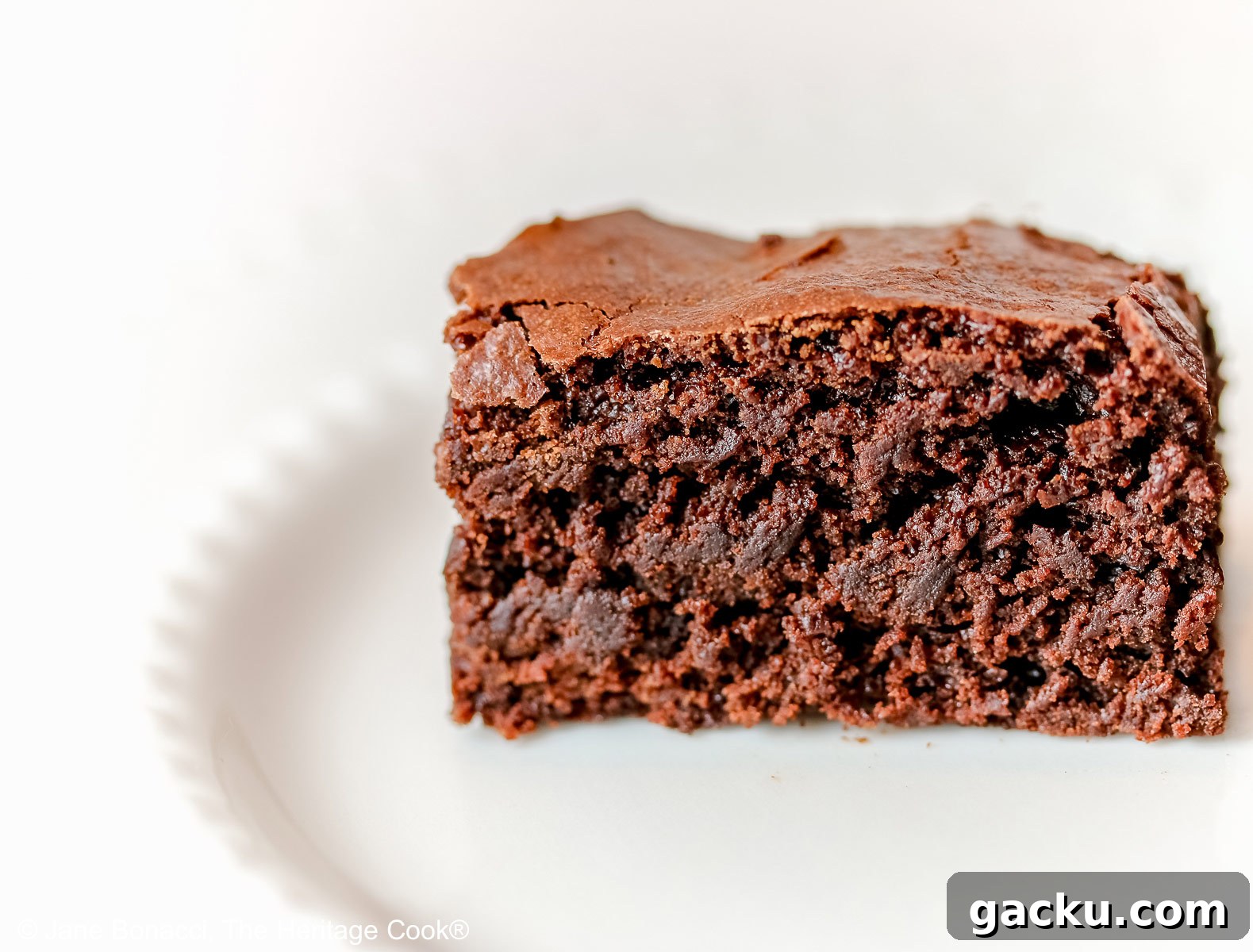 Close up of the side view of a single brownie on a white plate. 