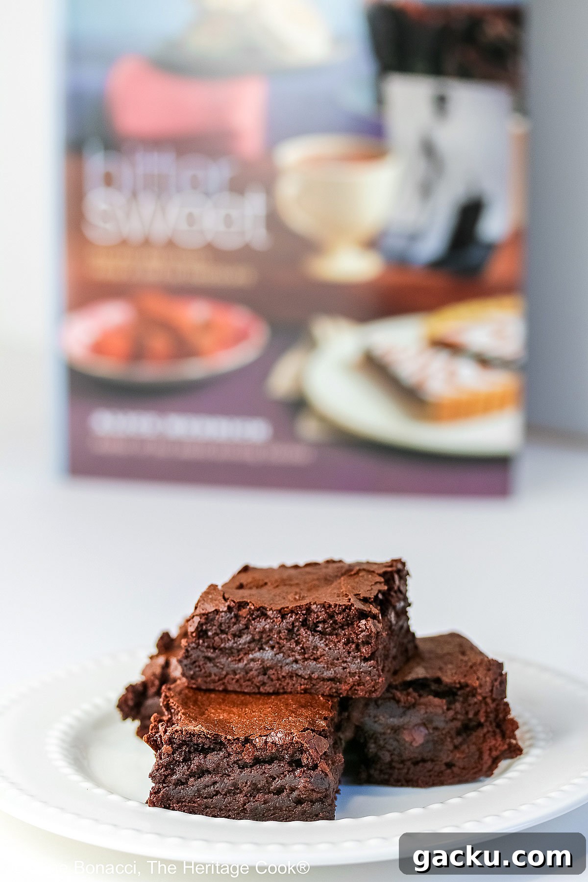 The Best Chewy Brownies, rich and so chocolatey, stacked on a white plate with two rows of white pearls, sitting on a white background; some shots of the cookbook, “Bittersweet” by Alice Medrich; © 2025 Jane Bonacci, The Heritage Cook.