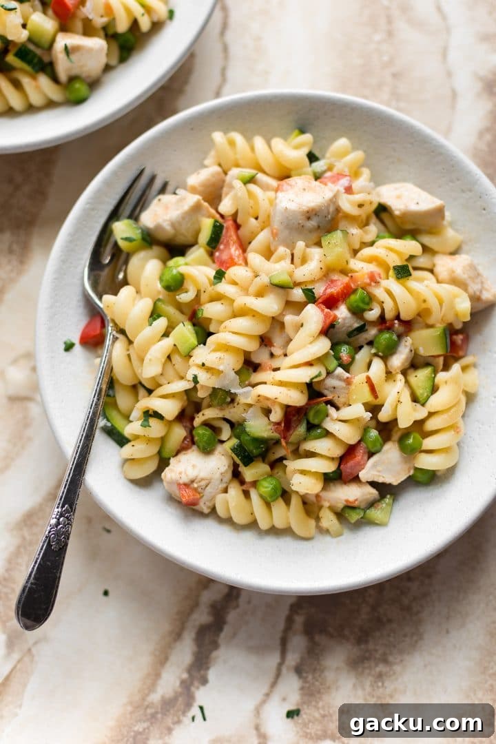 creamy chicken pasta primavera with fresh vegetables in white bowl with a fork