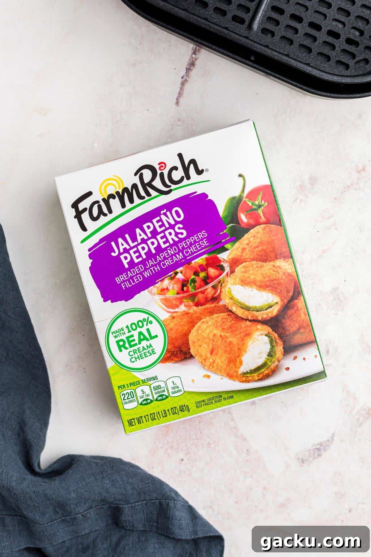 One box of frozen jalapeno poppers with an air fryer basket on a marble table. 