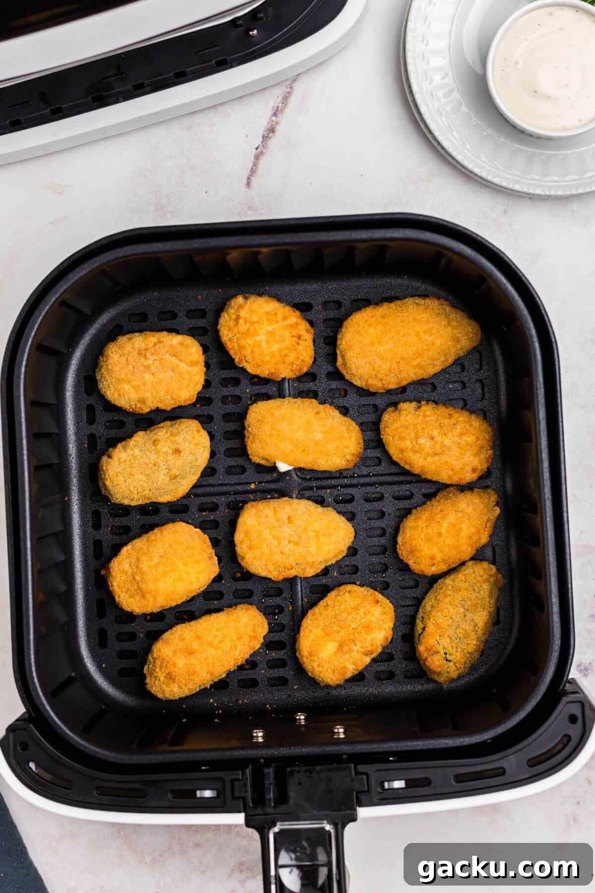 Golden crispy breaded jalapeno poppers in the air fryer basket after being cooked. 