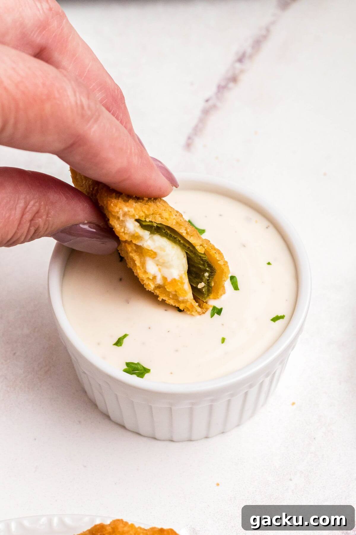 Golden crispy breaded jalapeno popper being dipped into ranch dressing. 
