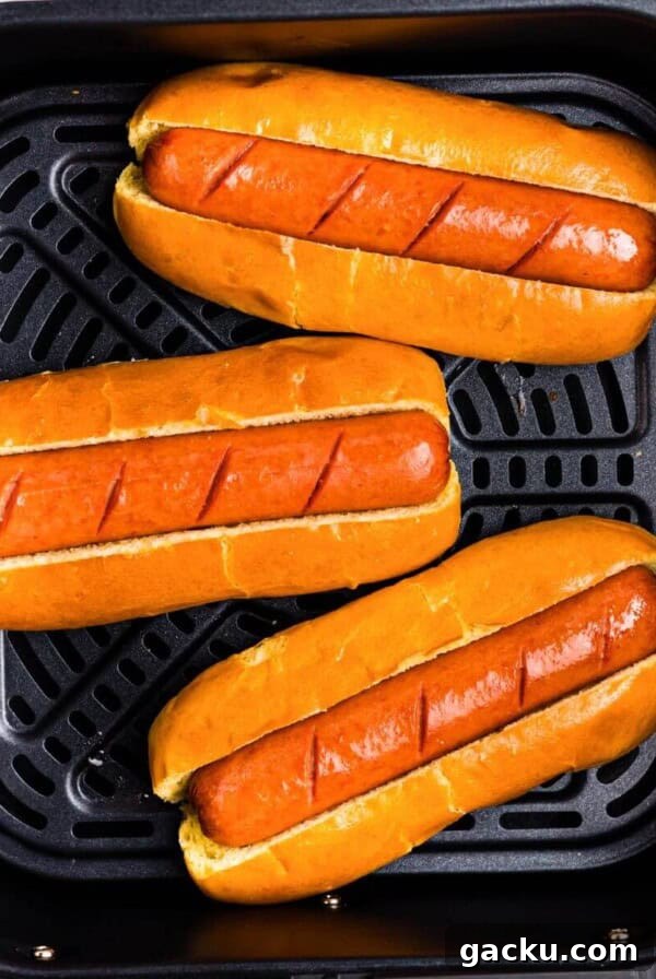 Juicy brown hot dogs in buns in the air fryer basket.