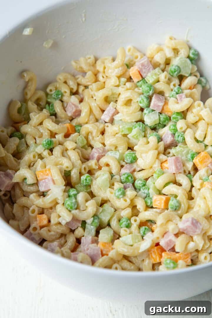 Cheesy Ham Macaroni Salad with Sharp Cheddar 6 cooked macaroni tossed with peas, ham, and cheddar in a white bowl.
