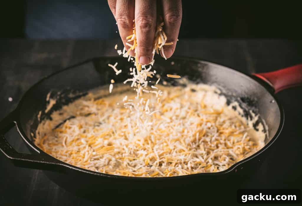 Skillet Bacon and Smoked Cheese Dip Recipe 3 Cheddar jack being sprinkled on top of a skillet of dip.