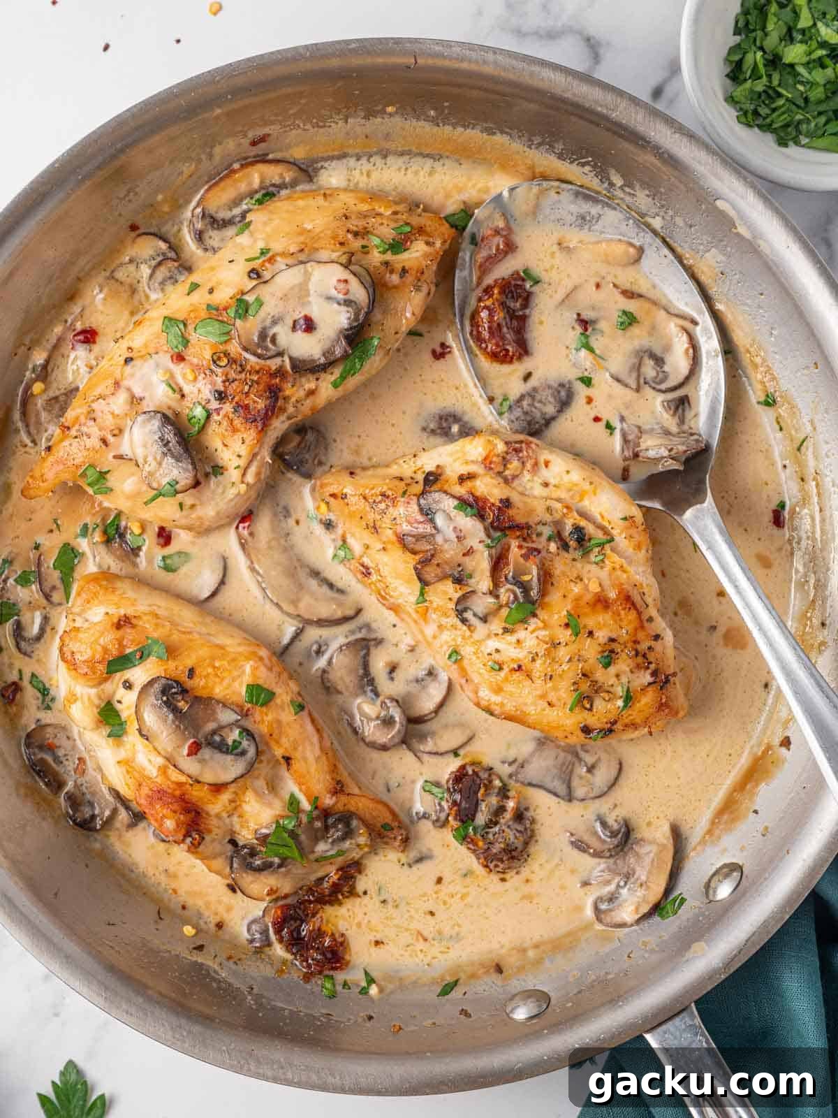 A spoon ladles marsala cream sauce over stuffed chicken breast.
