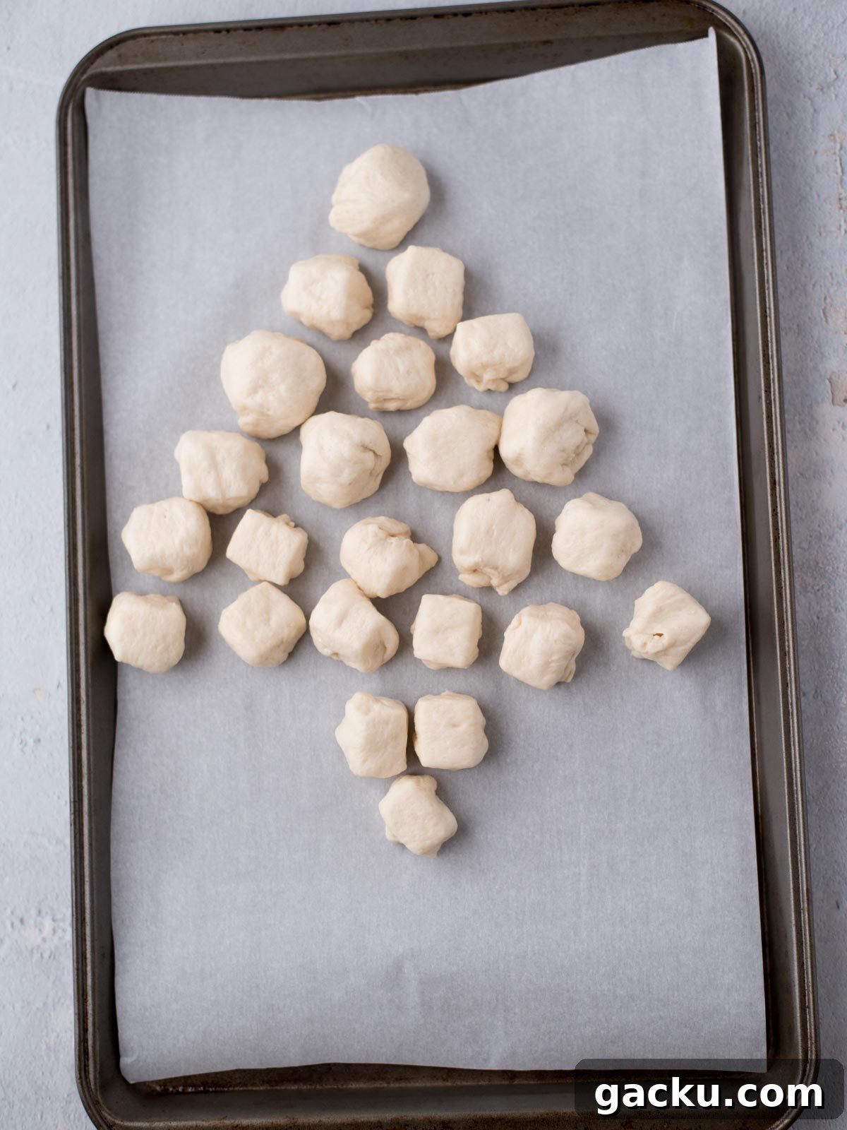 Christmas Tree Pull-Apart Bread Recipe for Holiday Brunch 5 Small pieces of dough are arranged in the shape of a Christmas tree on a baking tray lined with parchment paper.