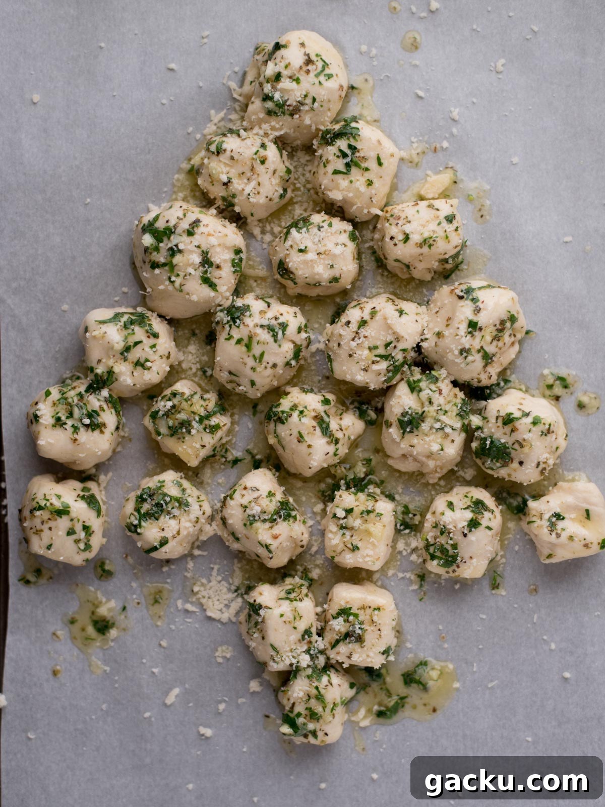 Christmas Tree Pull-Apart Bread Recipe for Holiday Brunch 6 Balls of dough topped with chopped herbs and grated cheese are arranged on a baking sheet in the shape of a Christmas tree.