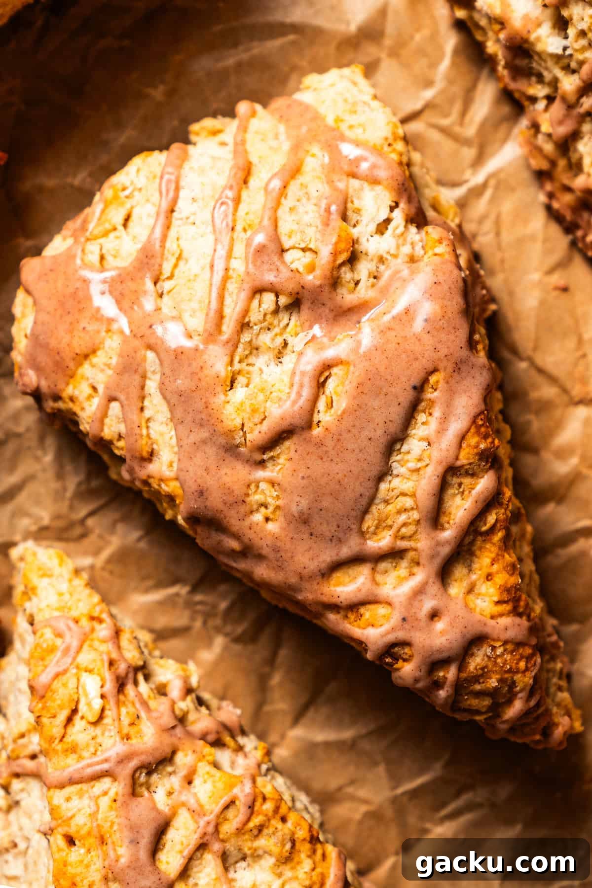 These tender, flaky cinnamon scones are packed with wholesome oats and cozy fall spice! Overhead close-up of a glazed cinnamon scone set on a sheet of brown paper.