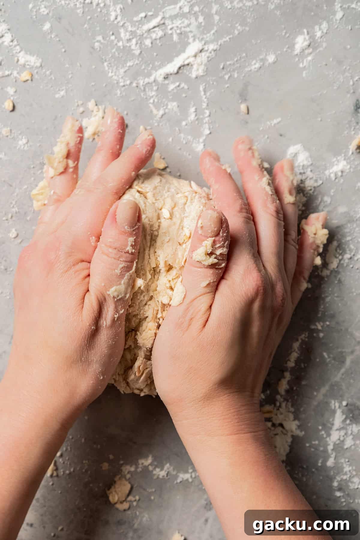 Knead the dough. Two hands kneading scone dough on a floured countertop.