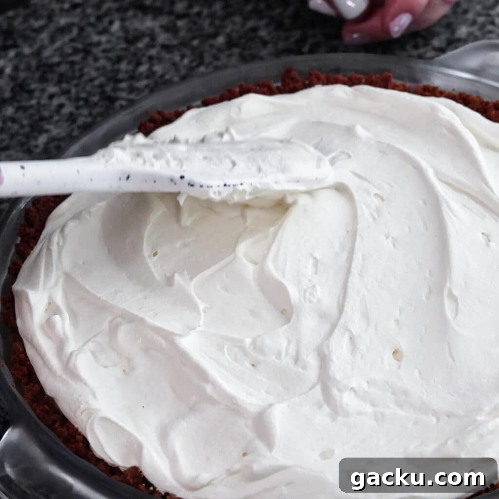 Gluten-Free Lemon Pie Recipe: Zesty Tart with Buttery Crust 13 smoothing whipped cream on top of pie using a silicone spatula.