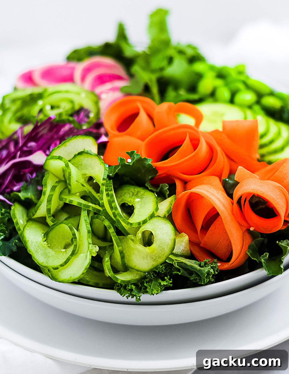 Sesame Ginger Salad Dressing Recipe for Crisp Greens 3 A large white bowl with kale, cucumbers, carrots, radishes, and red cabbage inside.