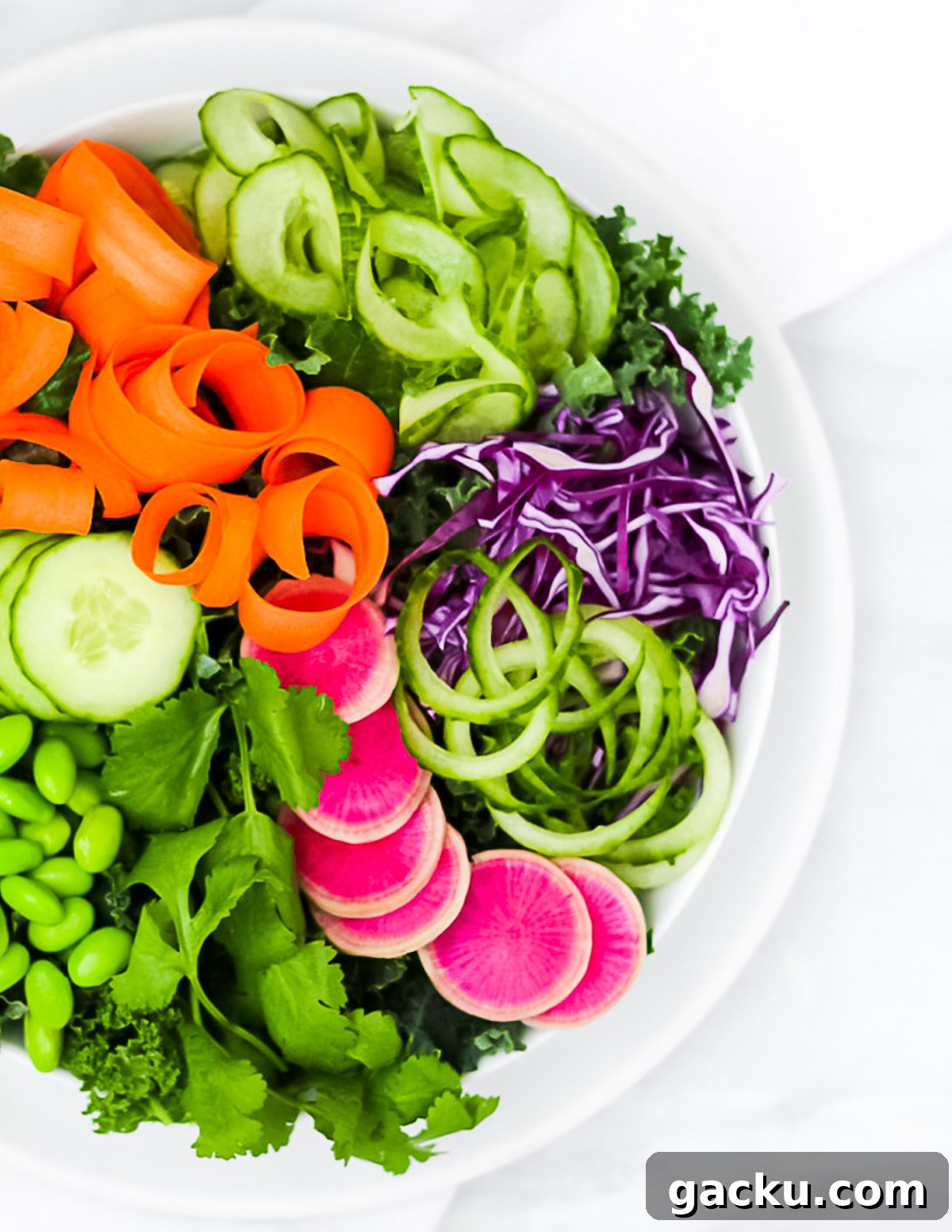 Sesame Ginger Salad Dressing Recipe for Crisp Greens 5 An overhead picture of a salad in white bowl. The salad includes kale, cucumbers, carrots, red cabbage, pink radishes, edamame, and cilantro