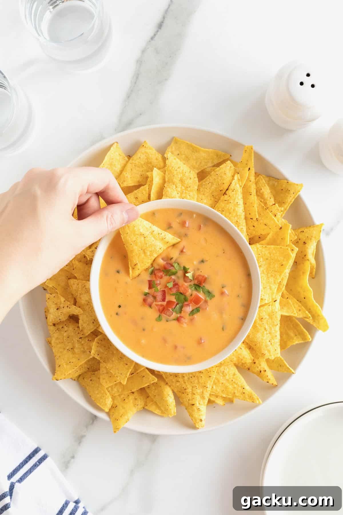 Stovetop Queso Recipe: Creamy, Quick Melted Cheese Dip 2 A bowl of queso in the middle of a large white round serving platter filled with corn tortilla chips.