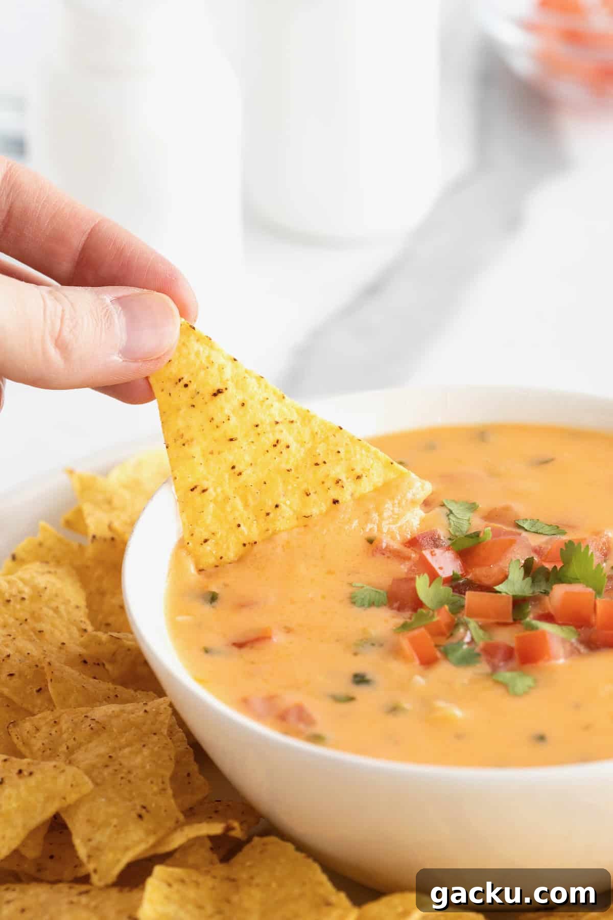 Stovetop Queso Recipe: Creamy, Quick Melted Cheese Dip 3 A hand dipping a corn tortilla chip into a white serving bowl of queso.