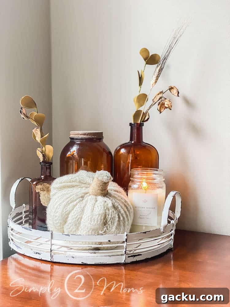 15 Fall DIY Home Decor Crafts to Transform Your Space 12 A round metal tray with handles painted with chipping paint holds a handmade sweater pumpkin, a burning Antique Candle Co candle, and three pieces of vintage amber glass