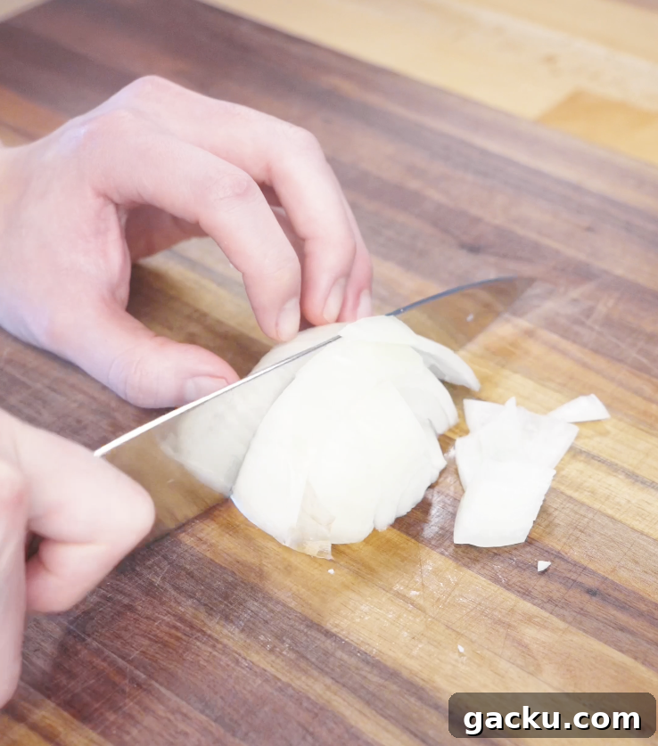 Slicing a white onion into thick wedges on a wooden cutting board to prepare vegetables for garlic chicken stir fry.