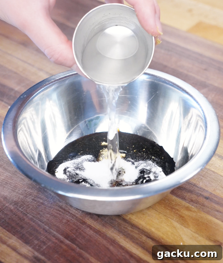 Pouring water into a bowl with soy sauce, oyster sauce, sugar, and chicken bouillon to create the savory garlic stir fry sauce.