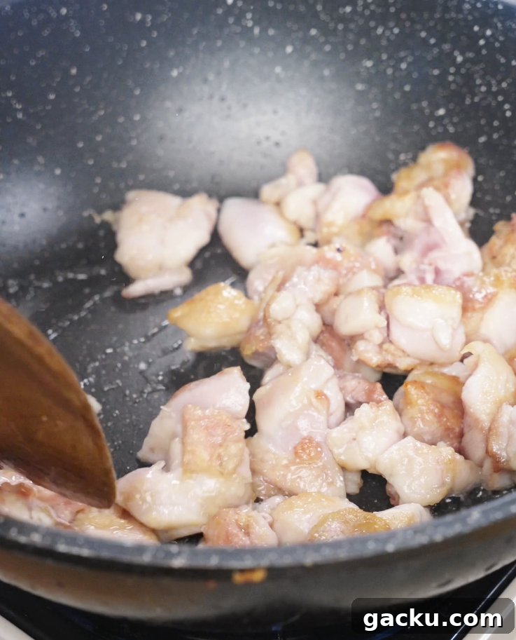 Chicken thigh pieces browning in a nonstick pan to develop flavor before being tossed with garlic and vegetables.