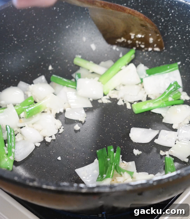 Sautéing minced garlic, onion wedges, and scallion whites in a pan to build the aromatic base for garlic chicken stir fry.