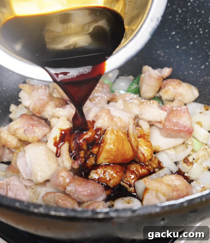 Pouring prepared soy garlic sauce over browned chicken and aromatics as it begins to thicken and coat the stir fry.