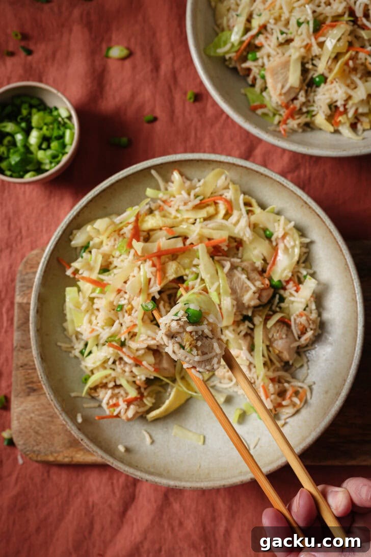 Indo-Chinese Basmati Fried Rice Recipe 20 Holding a spoonful of Chicken Fried Rice with chopsticks over a partially eaten plate.