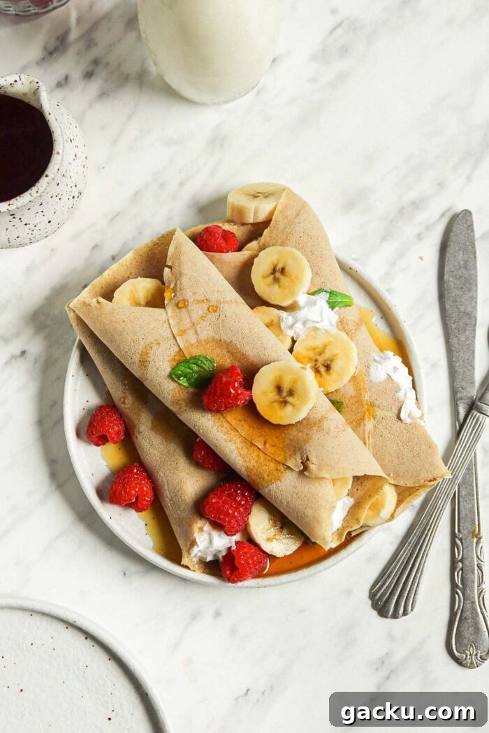 Overhead view of 3 buckwheat crepes filled with strawberries, banana and whipped cream on a plate.