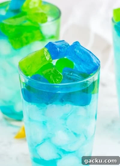 Three glasses of turquoise Jolly Rancher Cocktail with jolly rancher candy on marble countertop.