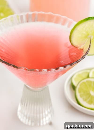 Decorative glass with Pink Flamingo Drink garnished with a lime next to a dish of limes.