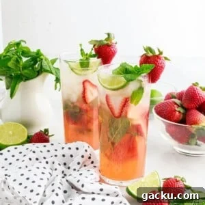 Two Strawberry Mojitos with a bowl of mint and strawberries.