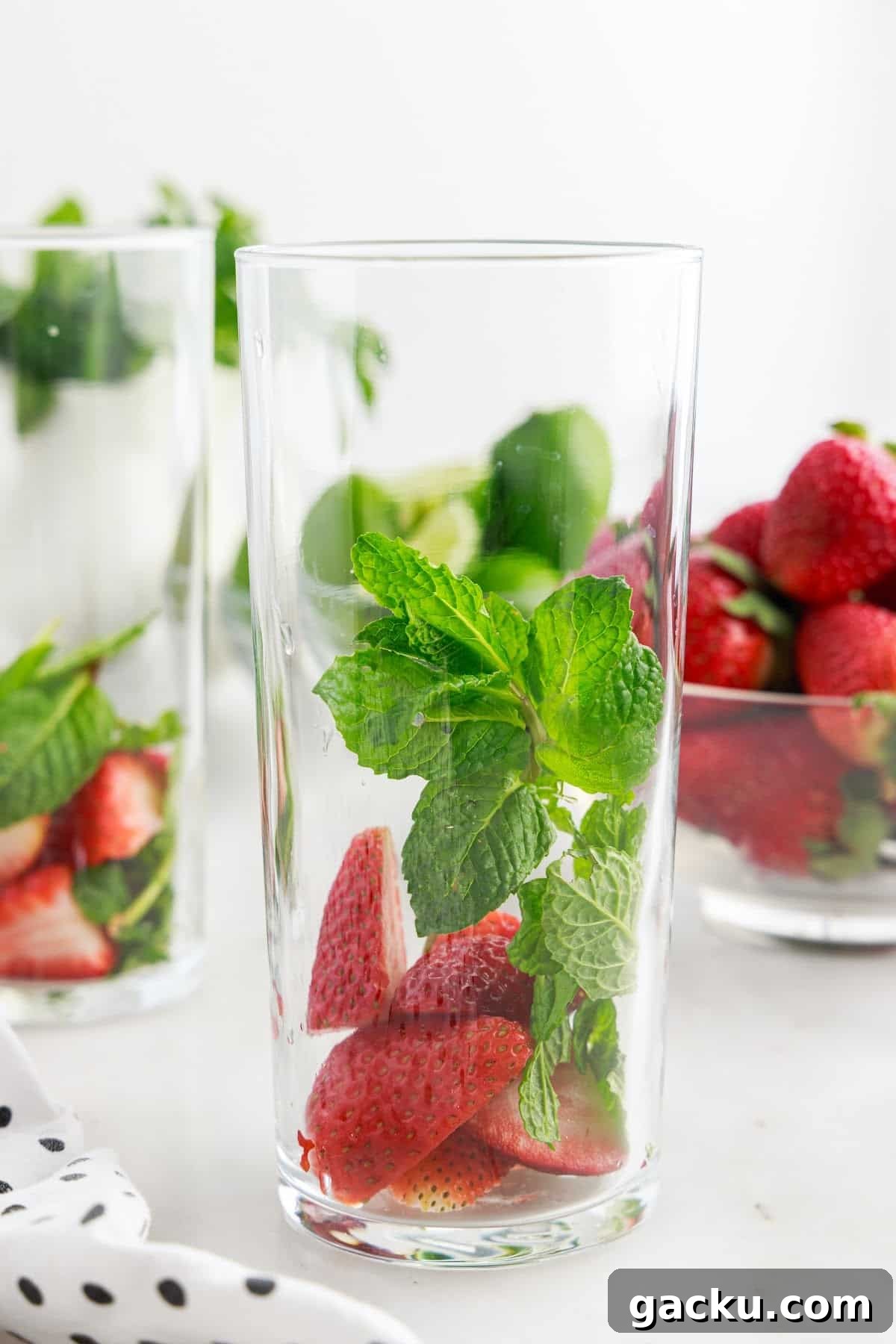 A tall glass with strawberries and mint in it.