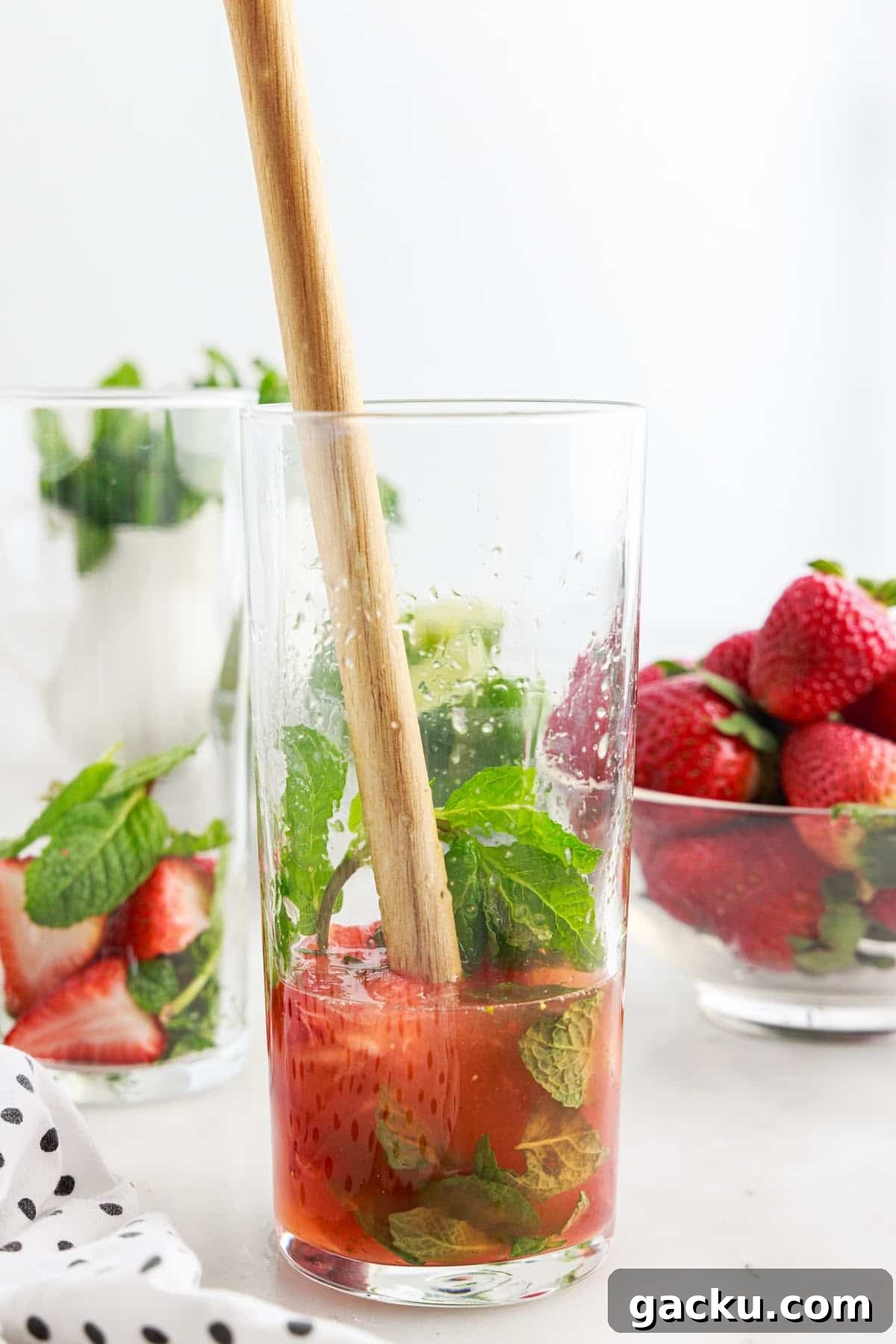 Mint, lime, and simple syrup being muddled in a glass.