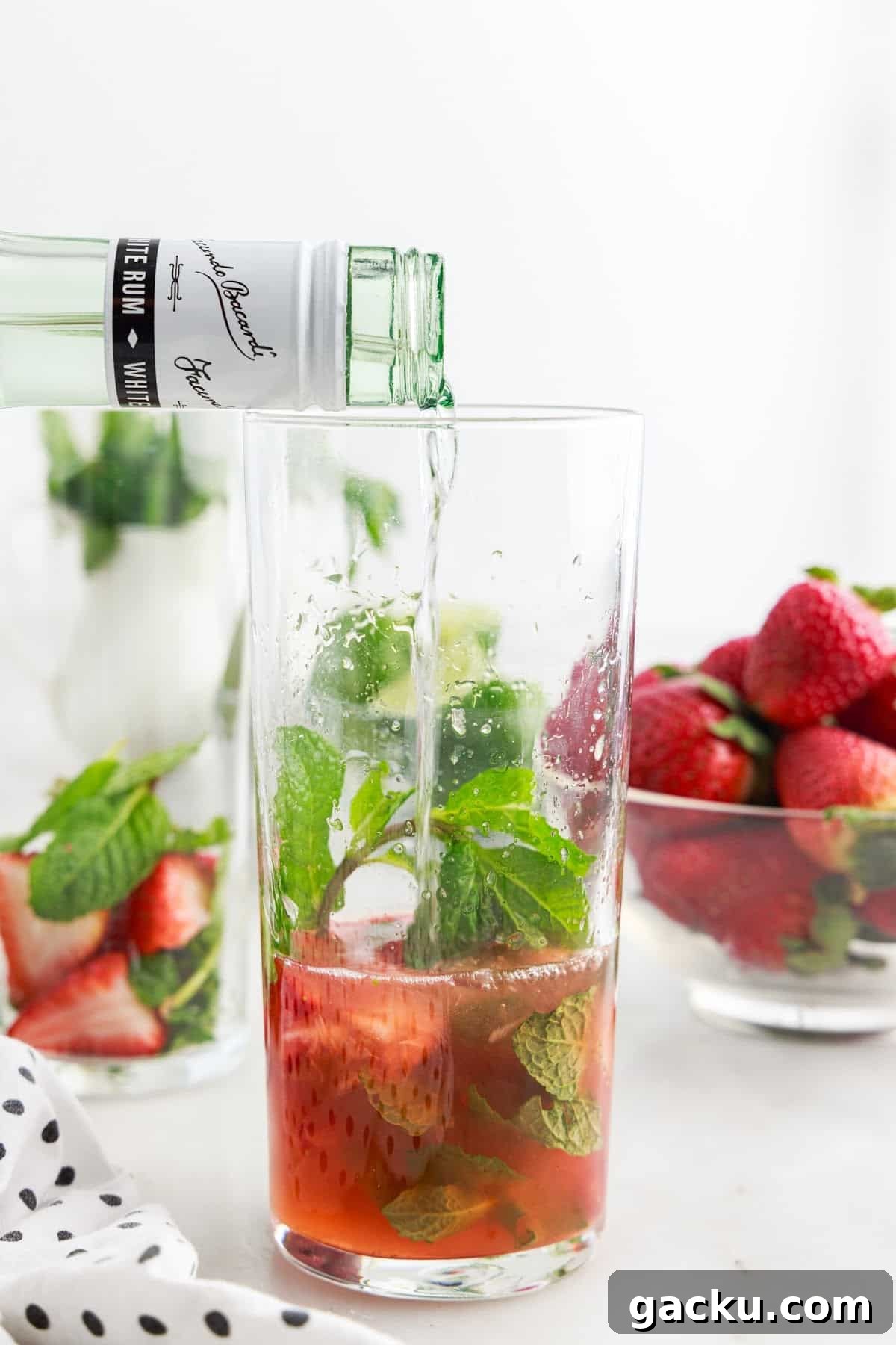 Rum added to ingredients in a tall glass to make a Strawberry Mojito.