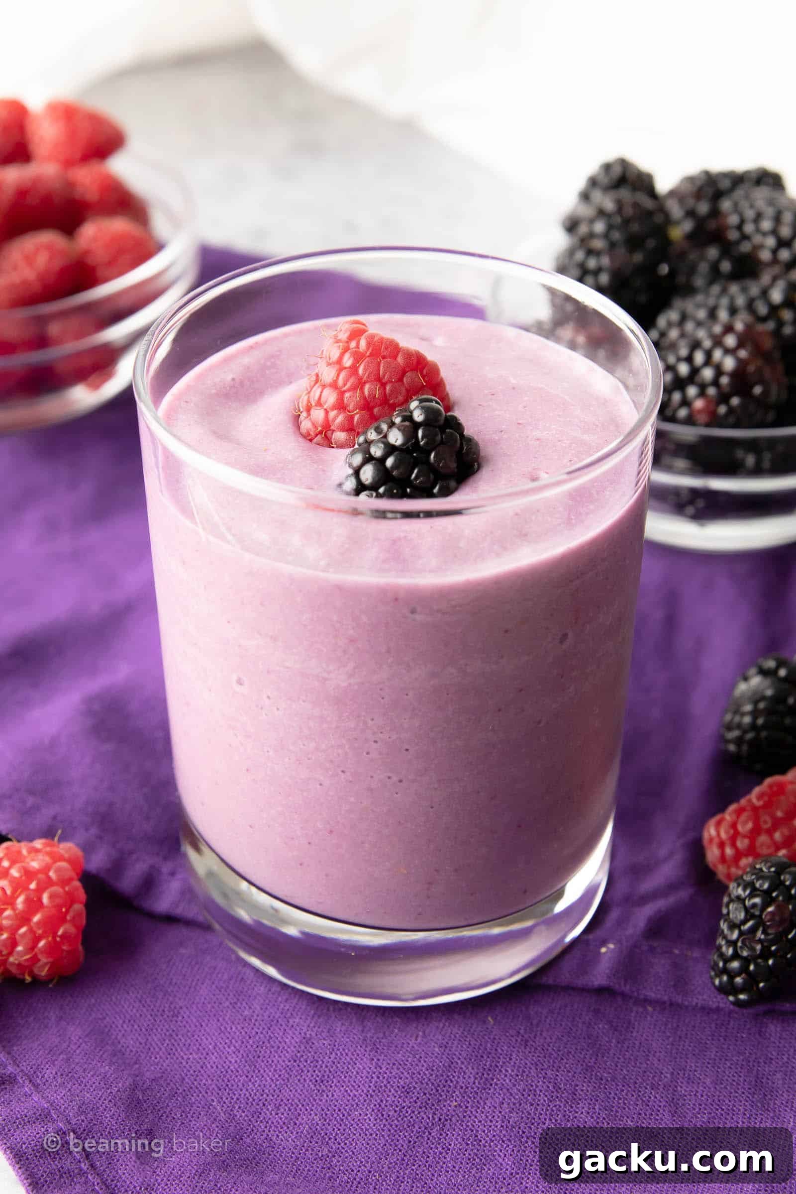 Glass of keto berry smoothie on a purple cloth with cups of fruit in the background