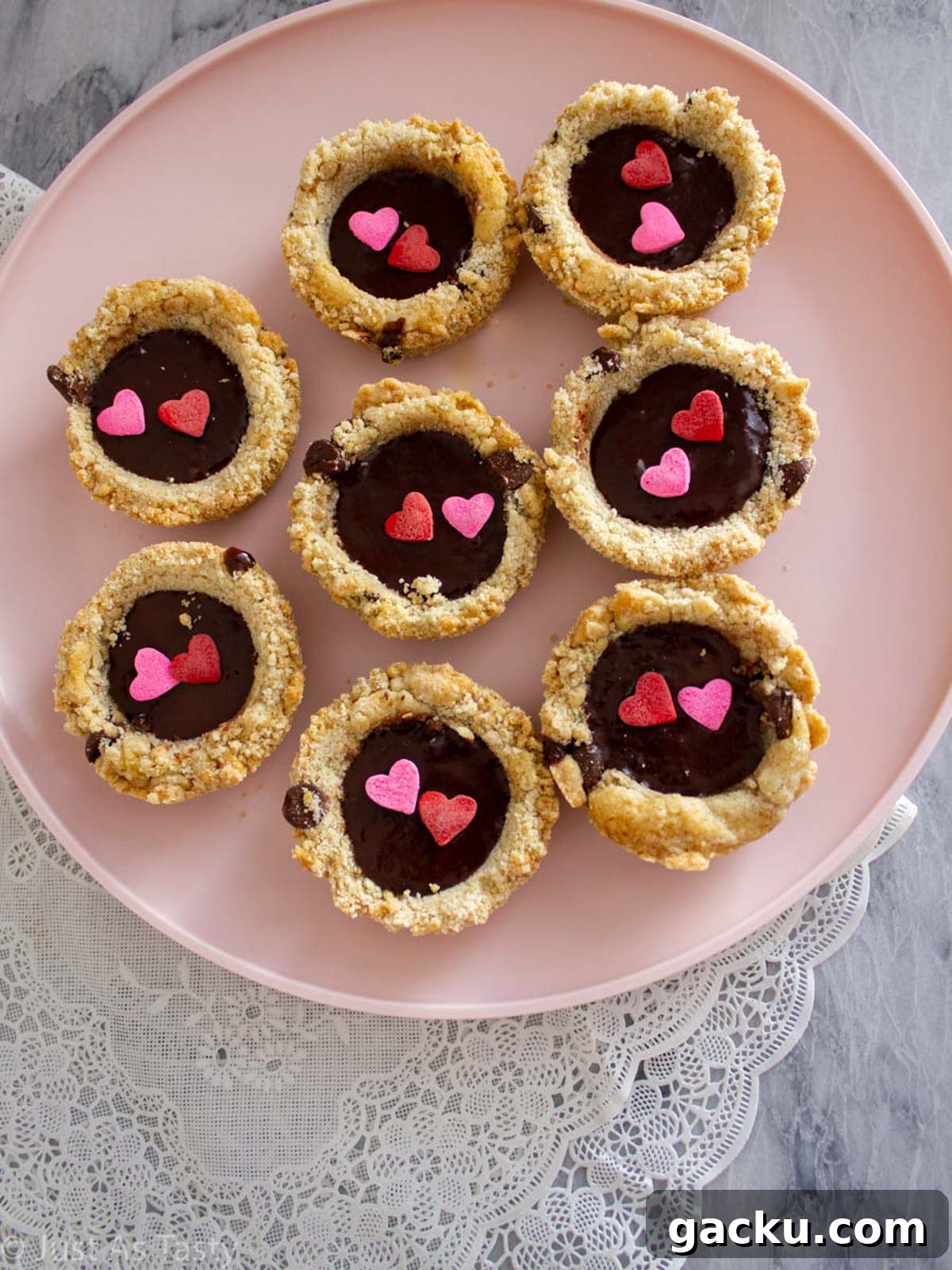 Chocolate Chip Cookie Cups Recipe — Mini Baked Cookie Desserts 5 Chocolate chip cookie cups filled with chocolate ganache on a pink plate.