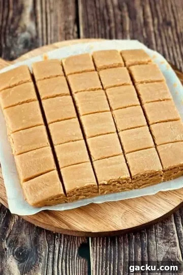 Creamy peanut butter fudge cut into small squares on a round cutting board.