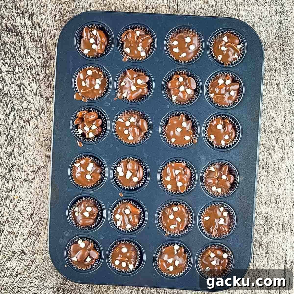 The chocolate clusters in a muffin tin topped with mini white chocolate chips.