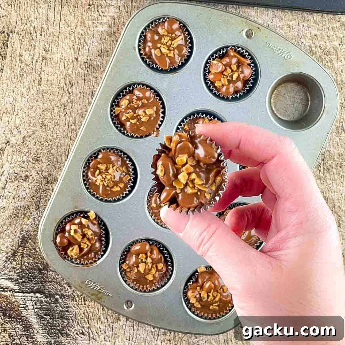 A hand holding a peanut cluster in a muffin liner.