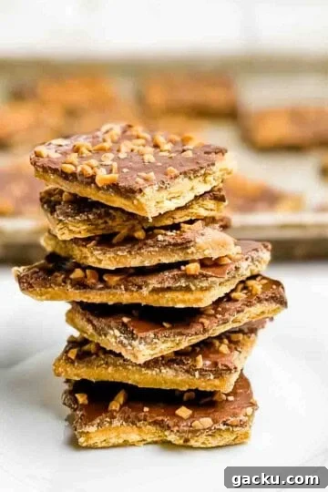 Seven pieces of christmas crack stacked on a white plate, with a tray of christmas crack behind it in a sheet pan.
